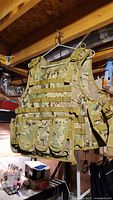 Front side of multi-cam airsoft tactical vest showing four pouches with flap covers and adjustable shoulder straps.