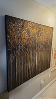 Side angle view highlighting the depth and texture of the large abstract painting showing white tree branches on brown and metallic gold background.