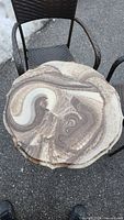View of the round table top showing the marbled stone pattern in beige, brown, and cream colors, and part of a wicker chair seat.