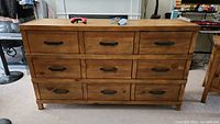 Front view of wooden dresser showing 9 drawers with metal handles and natural wood finish.