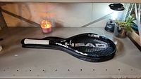 Full view of Head tennis racket beside the candle on a metal table, showing the racket in its black carrying case.