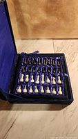 Blue velvet lined case open with black and white chess pieces arranged inside