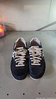 Front and top view of a pair of navy blue Saucony men's shoes with white laces and soles shown on a grey surface.