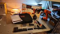 New Black + Decker 20V lithium ion cordless drill kit and accessories laid out on table showing drill, bits, charger, carrying case, and instruction manual.