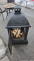 Side view of black metal fire pit showing domed top and door open with wood inside