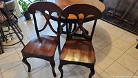 Two dining chairs with carved wooden backs and seats, matching table finish