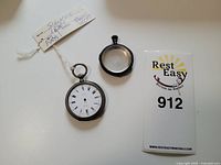 Photo showing the pocket watch and its separate outer case with a glass cover, along with a tag indicating .800 silver and origin Paris.