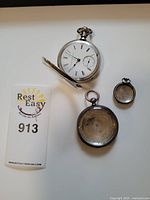 Three .800 silver pocket watches and a silver watch case displayed flat on white surface with an auction tag.