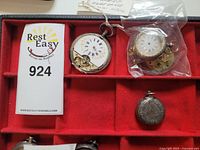 Photo showing silver pocket watch cases and parts in a red display tray with auction label 924