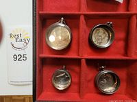 Four silver pocket watch cases arranged on red velvet display. Cases are empty and show various designs.