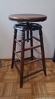 Full view of barstool showing round seat, four turned legs, stretchers, and adjustable screw mechanism