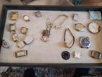 Overview of 23 items including various Bulova watch faces, parts, movements, and incomplete watches laid out on a flat surface.