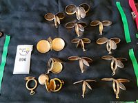 Top-down view of sixteen gold filled and gold plated pocket watch cases arranged on a black cloth surface showing their hinged open covers.