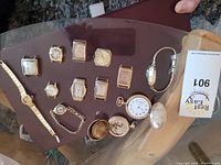 Photo showing 10 gold plate and gold filled wrist watches and 2 gold pocket watches arranged on a table.