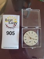 Front view of watch movement in acrylic box with dial and auction card