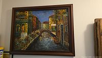 Full view of the framed oil painting portraying a Venice canal with buildings and a bridge.