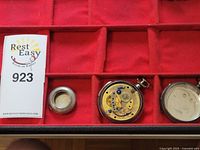 Full view of pocket watch cases and one pocket watch movement surface in a red lined box