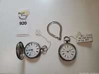 Two open-face pocket watches and snake chain laid flat, one watch case open showing enamel dial and subsidiary seconds