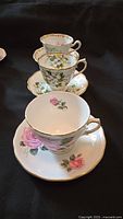 Side view of four stacked teacups and saucers showing floral patterns and gold trim.