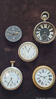 Top-down view of all five vintage clocks on dark fabric background.