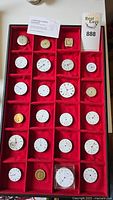 Overall view of 23 assorted watch faces and movements placed in red velvet display case.