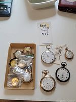 Overview of five pocket watches arranged next to a tray with loose movements and dials