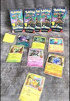 Photo shows five sealed Pokémon Trick or Trade card booster packs and nine loose Pokémon cards arranged on a gray textured surface.