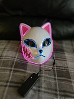 Front view of white fox mask illuminated with blue and pink LED lighting, showing battery pack and chin guard