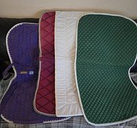 Four assorted equestrian saddle blankets stacked on a surface showing color and pattern variety.