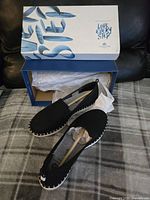 Pair of black women's slippers displayed with original Cloudsteppers by Mark's box. Shoes containing wooden shoe stretchers to maintain shape.