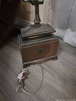 Close-up view of the lamp base showing metal ornamental detailing and the power cord wrapped beside it.