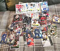 Top-down photo showing an assortment of hockey cards from different NHL players and teams laid out on a blanket surface. Cards include various designs, some glossy, some holographic.