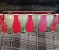 Four Coca Cola drinking glasses in original red packaging shown from front.