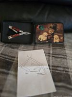 Ducks Unlimited multi-tool open in metal tin next to an instruction sheet with tool labels