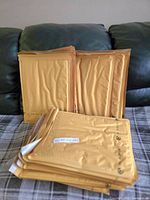 Stack of 25 brown padded envelope mailers arranged on a fabric surface.