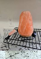 Salt lamp on a black metal rack showing the lamp unplugged with the power cord and dimmer switch beside it on a granite countertop.