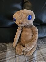 Front-facing photo of the vintage 1982 E.T. plush toy seated on a cloth surface, showing the full body and blue eyes.