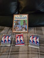 Photo of the Vintage TV Superstars Scrapbook with images of TV celebrities on the cover, placed on a surface, accompanied by three sealed NBA HOOPS 1990-1991 trading card packs.