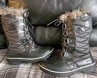 Side profile of the black women's SOREL winter boots showing quilted design, faux fur collar, metal lace hooks, and SOREL logo patch.