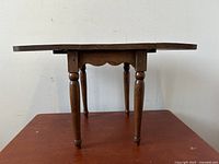 Side view of miniature wooden drop-leaf table with legs and extended leaf.