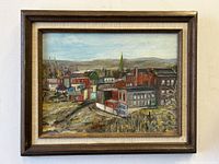 Framed oil painting showing a cityscape with buildings, a church steeple, and hills in the background.