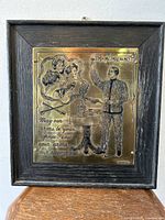 Front view of brass plaque in oak frame showing full embossed artwork and text.