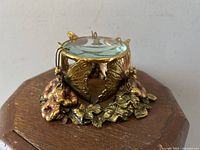 Front angled view of the small decorative holder with detailed metal butterflies and flowers supporting a glass magnifier.