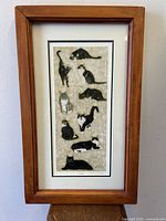 Full view of framed "Nine Lives" cat art print showing nine cats in various poses within a wood frame.