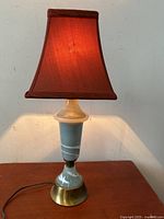 Lamp illumination photo showing red fabric shade lit and emitting warm glow with blue marbled glass base on wooden surface.