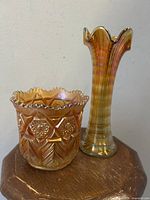 Two antique carnival glass pieces on wooden surface; orange-yellow iridescence, one stretch vase and one spooner.