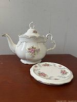 Teapot and trivet side view showing floral and gold detailing on both pieces placed on brown wooden surface