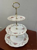 Front view of the three-tier cake stand showing floral designs and gold accents on porcelain plates.