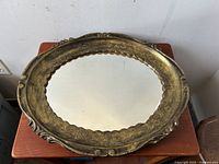 Top-down view of the oval gold-toned Florentine mirror showing the full frame and glass surface.