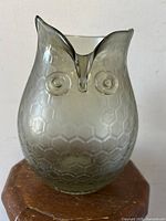 Front view of the owl-shaped glass vase showing the deep V-shaped opening, circular raised eyes, and honeycomb surface texture in smokey translucent glass.
